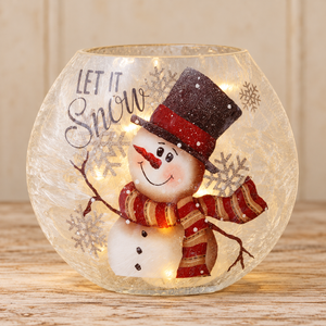 Frosted glass snowman luminary with a red striped scarf, dark top hat, and “Let It Snow” lettering on pale wood.