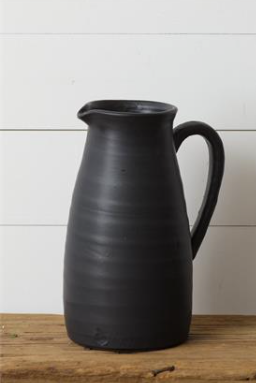 Tall matte black pitcher with a curved handle and pouring spout on a wooden surface.